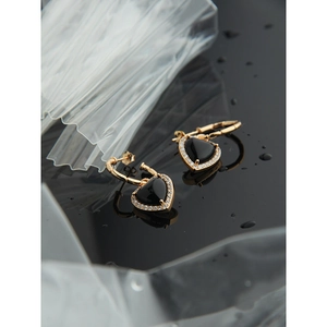 Macro detail of gold heart earrings with black onyx and sparkling white zircons