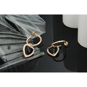Macro detail of gold bamboo-style hoop earrings with black heart-shaped pavé pendants