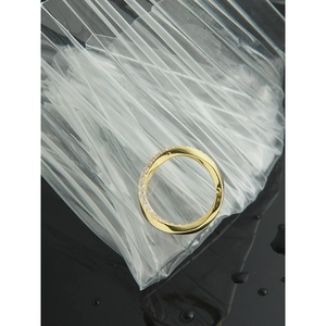Vue de dessus d'une bague Mobius dorée ornée de zircons sur sachets plastiques