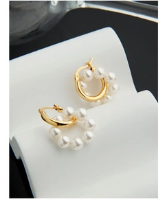 Détail de créoles dorées en forme de couronne avec perles sur support blanc