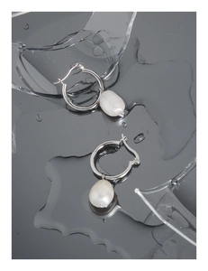 Macro shot of S925 silver hoop earrings with white baroque pearls on a wet mirror surface