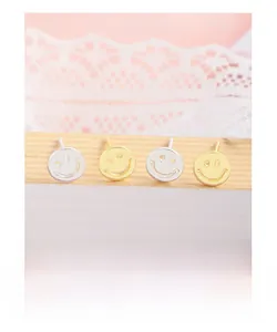 Close-up of minimalist gold and silver smiley face stud earrings on a wooden display