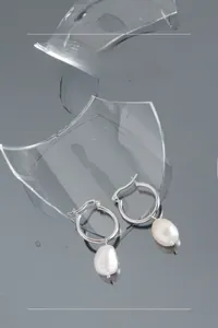Detail of S925 silver hoop earrings with irregular baroque pearl charms on a reflective surface