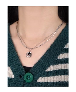 Detail of double-layer S925 silver necklace with black gemstone on green knitwear