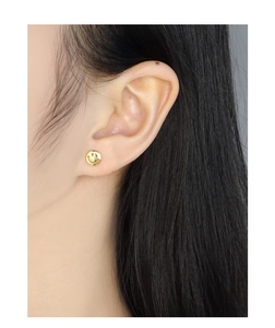 Detail of minimalist gold smiley face stud earrings worn by a model in a side view