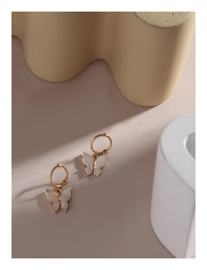 Close-up of butterfly hoop earrings featuring white shell texture pendants on gold hoops