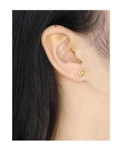 Close-up of a minimalist hollow smiley face stud earring worn on an ear for scale