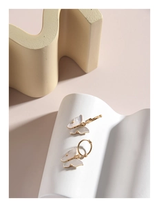 Detail showing shell butterfly pendant on golden hoop earrings with iridescent wings
