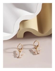 Macro shot of gold butterfly hoop earrings with iridescent shell texture on beige base