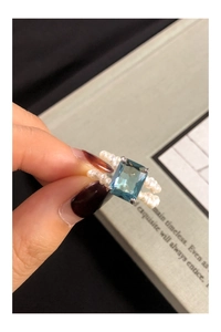 Detail of emerald-cut blue zircon and double-row pearl beaded ring on a green book