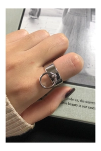 Polished silver wide band ring with a dangling round charm shown on a finger