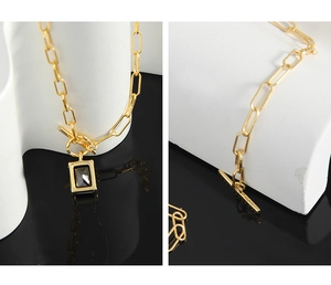 Detail of gold paperclip chain necklace with OT toggle clasp and black square pendant