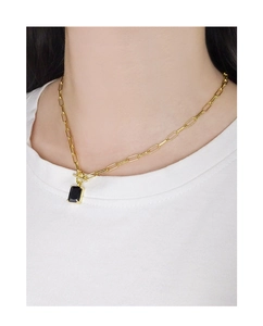 Detail of a minimalist gold paperclip chain necklace with a black rectangular pendant on a model