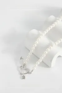 Macro detail of pearl necklace featuring heart pendant and silver arrow toggle clasp