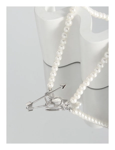 Macro shot of pearl necklace featuring silver heart and arrow toggle clasp on white pedestal