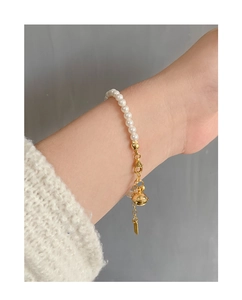 Gros plan d'un bracelet en perles argent S925 avec breloque cloche dorée au poignet