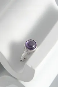 Close-up of minimalist silver ring featuring a round purple gemstone on stone background