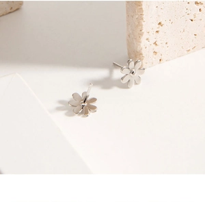 Macro shot of silver daisy stud earrings on stone texture showing polished 925 silver finish