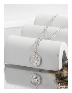Gros plan du collier chaîne trombone en argent avec un pendentif pièce de monnaie vintage