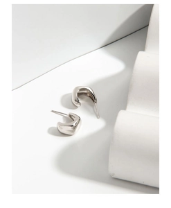 Close-up of minimalist S925 sterling silver chunky C-shaped stud earrings on white prop