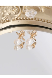 Macro detail of gold-plated knot earrings featuring zircon accents and teardrop pearls