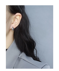 Macro side view of a polished silver teardrop stud earring worn by a model in a grey suit