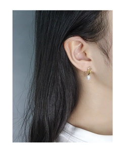 Detail of cross-bar gold earring with micro-pave zircons and white drop pearl on ear