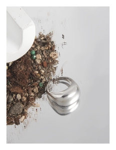 Macro shot of minimalist silver matte curved ring on a mirrored surface with natural decor