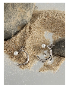 Detail of S925 silver C-shaped pearl earrings on a natural stone and mirror base