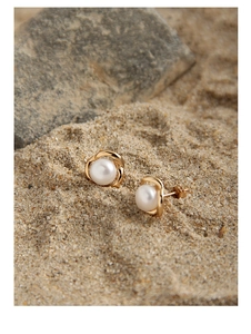 Close-up of pearl flower earrings with gold metal rings on a soft beach sand background