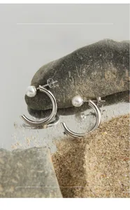 Macro shot of minimalist C-shaped S925 silver stud earring with a white pearl on a rock