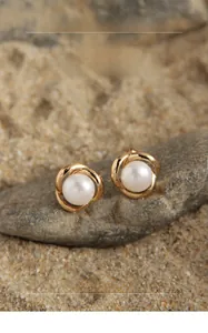 Macro detail of round white pearl earrings with golden flower settings on grey stone
