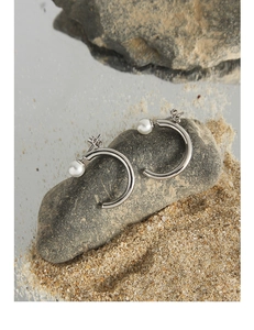 Detailed view of silver C-shape earrings with pearls on a natural stone background
