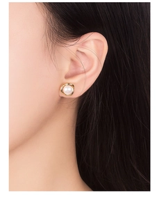 Detailed close-up of a white round pearl earring with elegant golden woven frame