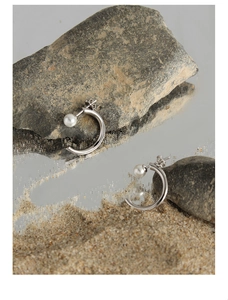 Detailed view of silver C-shape stud earrings with white pearl on a reflective surface