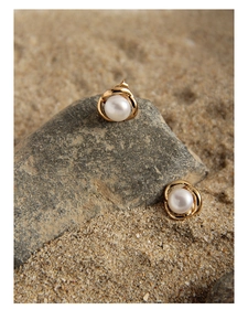 Detailed close-up of pearl stud earrings with gold twisted edge on sand and rock