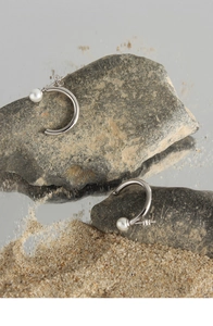 Macro view of C-shaped silver earrings with minimalist pearl design on natural stones