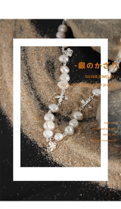 Macro detail of natural pearl necklace with silver flower and butterfly accents on sand