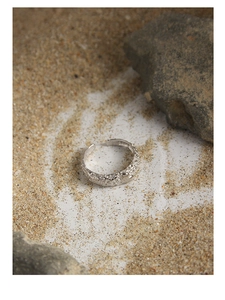 Detail of silver adjustable ring featuring hammered texture and a small heart on sand