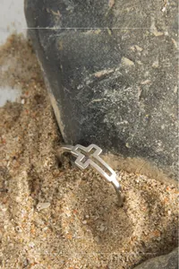 Detailed view of S925 sterling silver cross cutout ring on textured outdoor sand and rock