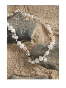 Detail of silver flower pendant and baroque pearls on necklace over beach sand