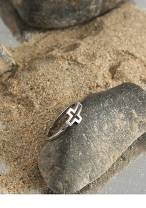 Detailed view of silver S925 geometric cross ring placed on natural grey rock and sand