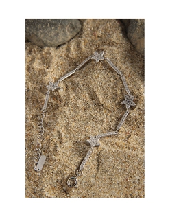 Macro detail of S925 sterling silver star bracelet with zircon inlay on sand rocks