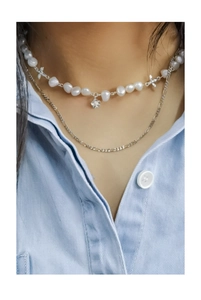 Detail of layered silver necklace with baroque pearls, flower and bow charms on a model