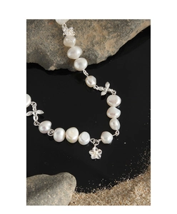 Detailed close-up of Baroque pearl necklace with silver flower and bee charms on dark stones