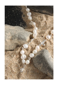 Close-up of baroque pearl necklace with silver flower pendant on a textured stone background