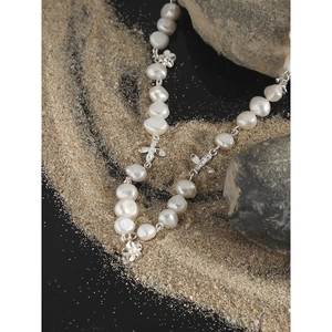 Baroque pearl necklace with silver flower and bow charms on natural stone background