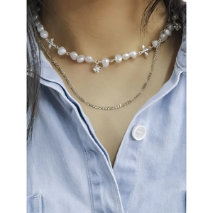 Minimalist silver flower and pearl layered necklace set on a blue denim shirt background