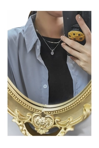 Close-up of double-layered silver necklace with oval sequin pendant on a model