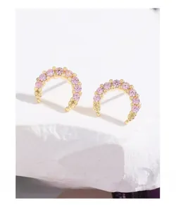 Macro shot of gold crescent earrings with pink pave-set zircons on a stone platform